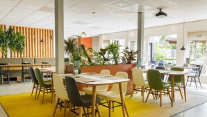 Un vaste espace intérieur aménagé en salle à manger, avec de nombreuses tables et chaises, un comptoir d’accueil et plusieurs plantes en pot.