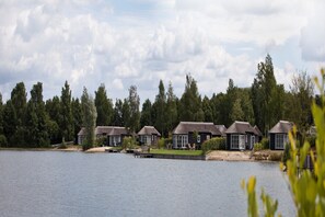 A lakeside hotel with multiple buildings, each featuring a thatched roof and large windows.