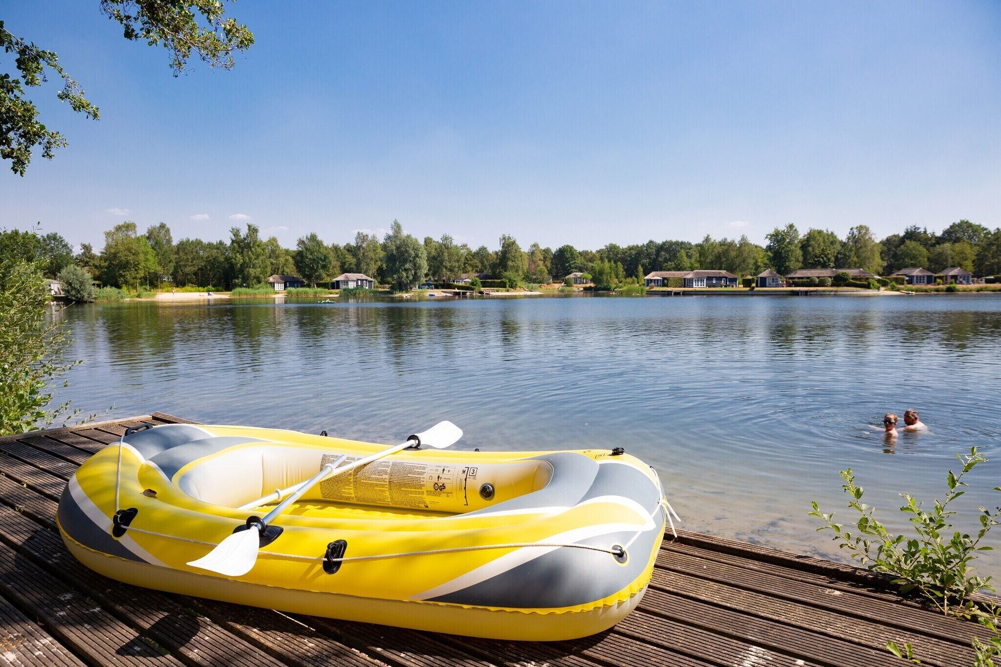A yellow inflatable raft on a wooden dock by a calm lake with houses in the background.
