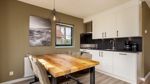 A modern kitchen with white cabinets, a wooden dining table, and a hanging light fixture. - Twente Steam Shower Holiday Home (Hoge Hexel)