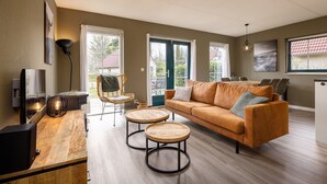 A modern living room with a sofa, two round wooden tables, a TV, and a lamp. - Twente Steam Shower Holiday Home (Hoge Hexel)