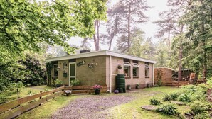 A rustic cabin with a brick exterior, surrounded by lush greenery and tall trees.
