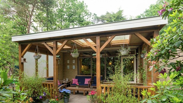 A covered patio with wooden furniture and hanging baskets.