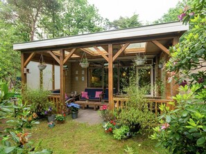 Une terrasse couverte, aménagée avec des meubles en bois et agrémentée de suspensions florales.