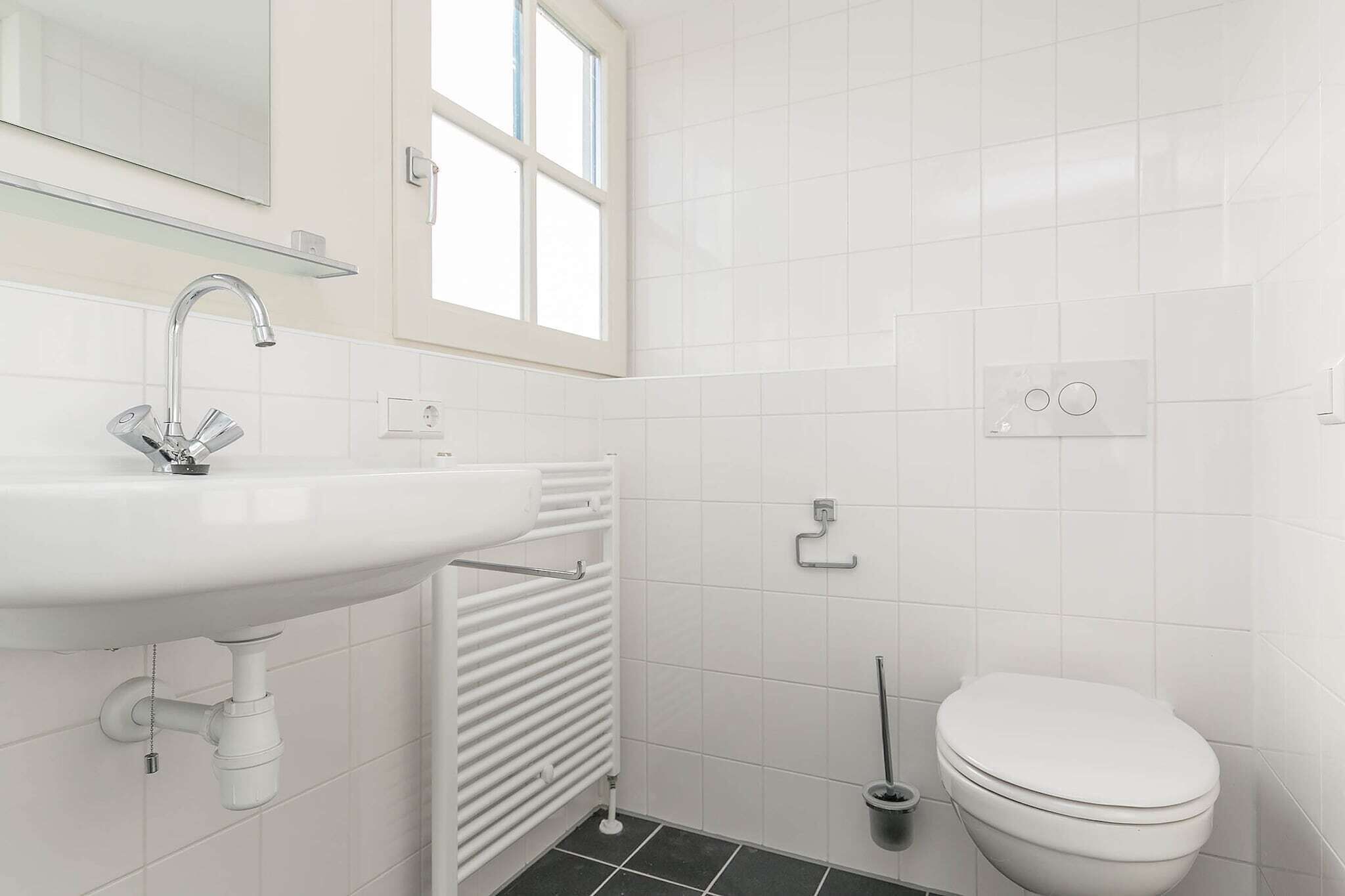 Casa de banho moderna com lavatório branco, sanita e radiador.