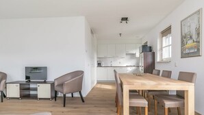 A modern living space with a dining area, kitchen, and a TV on a cabinet. - Villa Near Forest Trails (Hollandscheveld)