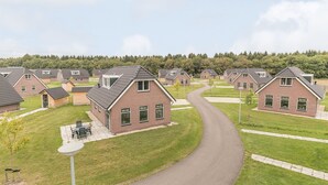 A residential area with multiple brick houses, a paved driveway, and a grassy lawn. - Villa Near Forest Trails (Hollandscheveld)