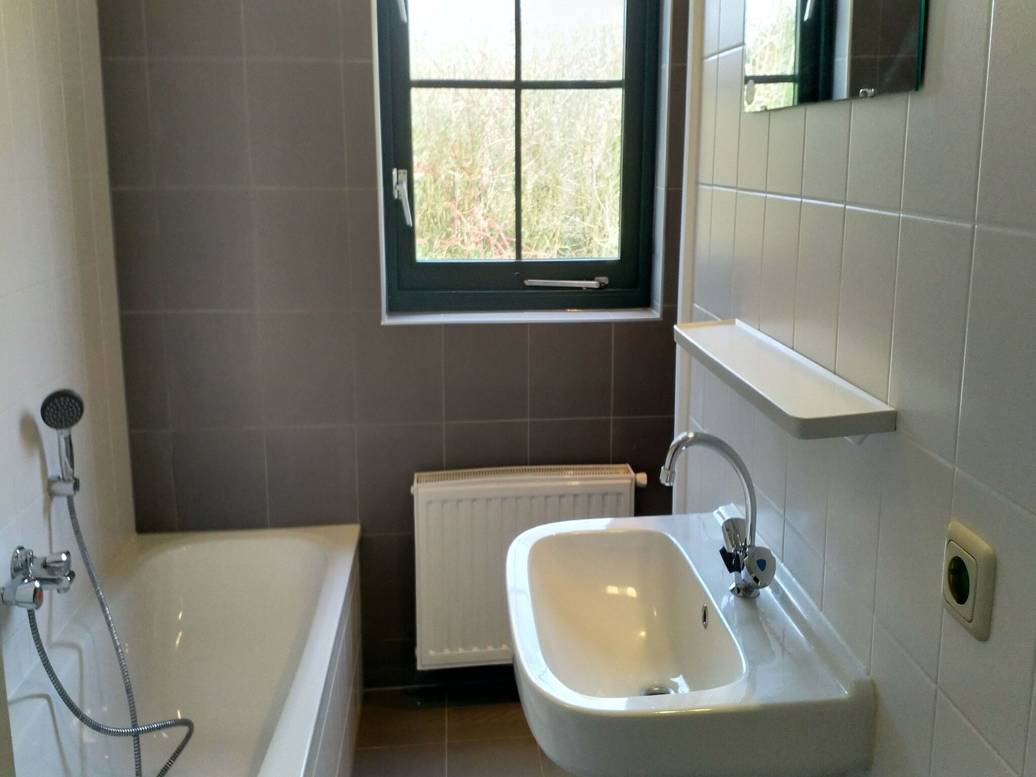 A bathroom with a bathtub, a sink, a window, and a radiator.