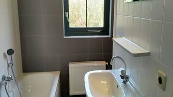 A bathroom with a bathtub, a sink, a window, and a radiator.