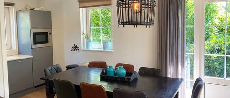 A modern kitchen with a built-in oven and microwave, a dining table with chairs, and a large window with curtains.