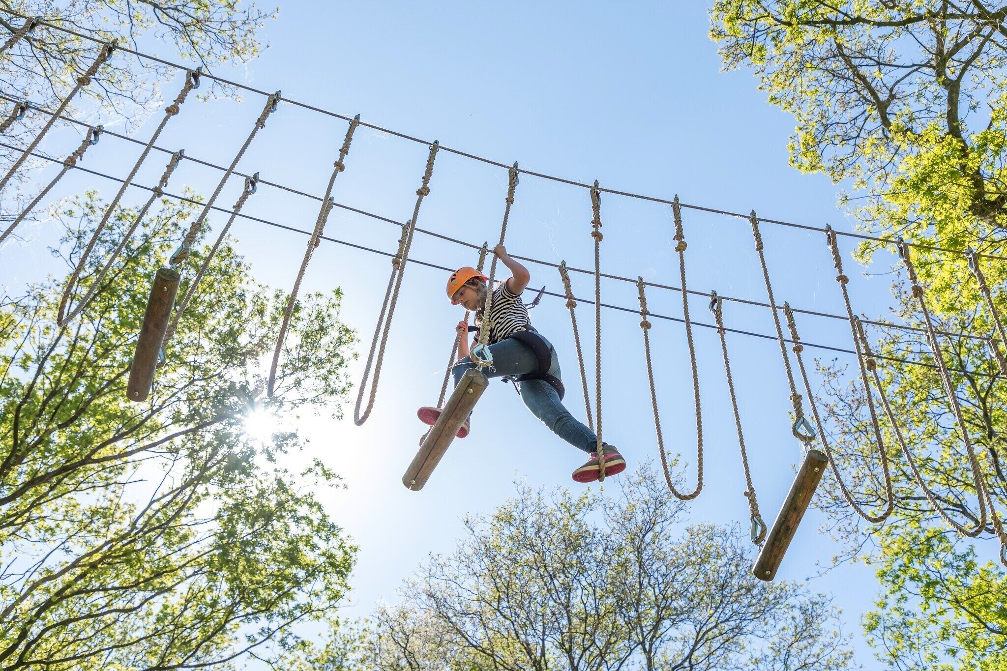 A person navigating an outdoor obstacle course with ropes and wooden planks.