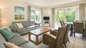 A living room with a sofa, coffee table, wicker chairs, a TV, and a painting on the wall.