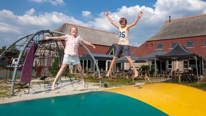 Two children jumping on a playground with a building in the background.