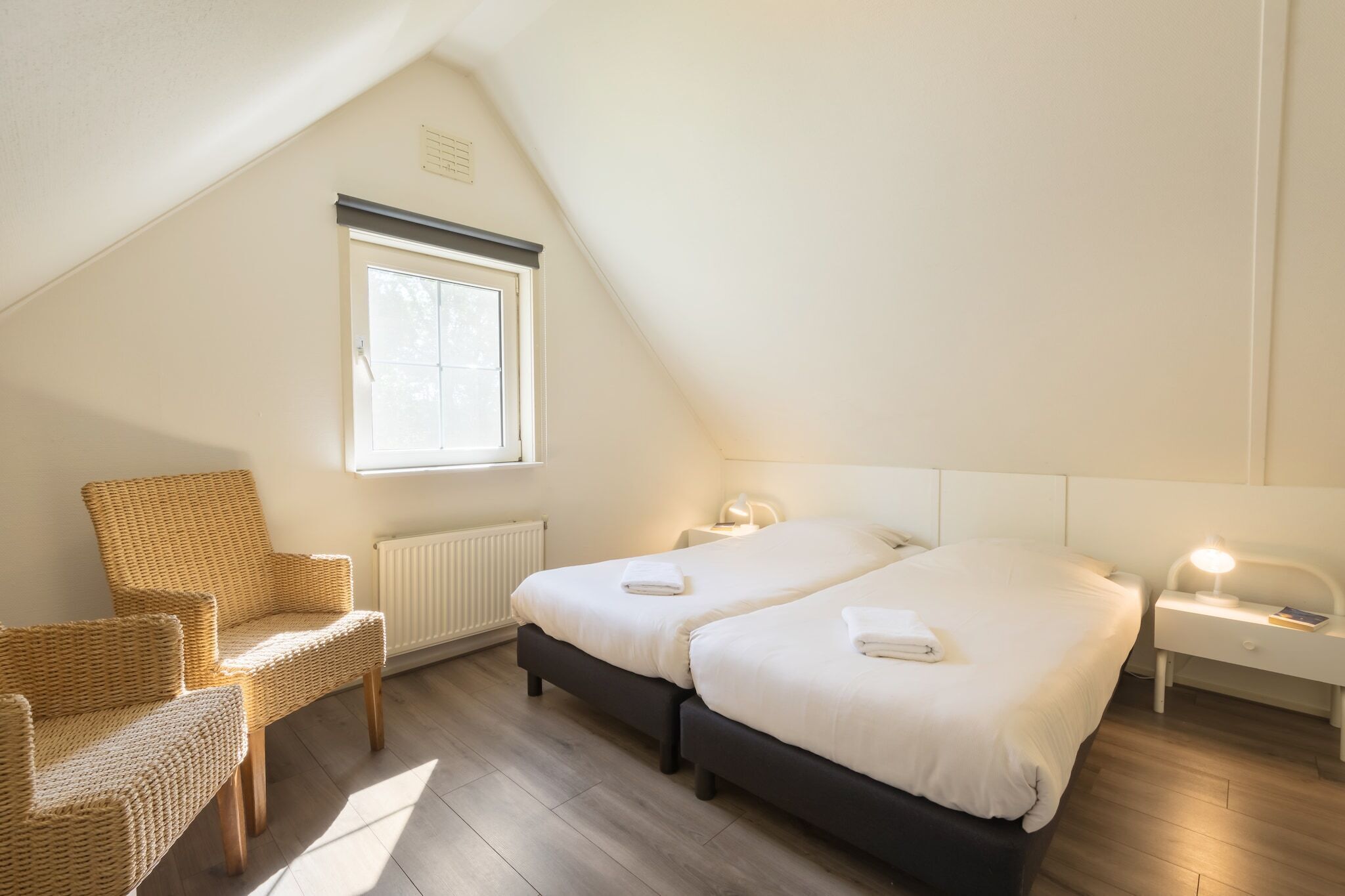 A bedroom with two beds, a chair, and a window.