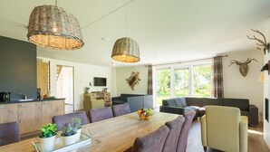 A modern living room with a wooden dining table, comfortable seating, and large windows. - Spacious Villa in a National Park (Paasloo)