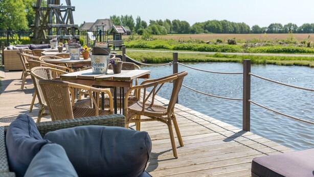 An outdoor seating area with wicker furniture and a view of a river. - Spacious Villa in a National Park (Paasloo)