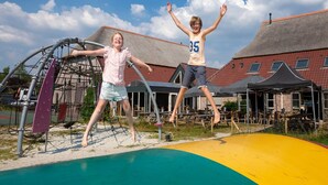 Two children jumping on a colorful playground with a building in the background. - Spacious Villa in a National Park (Paasloo)