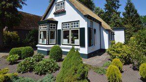 A traditional white building with a thatched roof, a bay window, and a small porch. - Holiday Home in Nijeberkoop near Nature (Nijeberkoop)