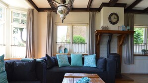 A cozy living room with a dark sofa, teal cushions, a wooden coffee table, and a vintage-style ceiling light. - Holiday Home in Nijeberkoop near Nature (Nijeberkoop)