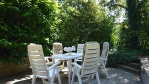 An outdoor patio with white chairs and a table, surrounded by lush greenery. - Holiday Home in Nijeberkoop near Nature (Nijeberkoop)