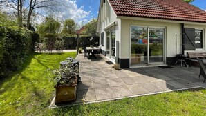 Una casa de dos pisos con techo de tejas, un patio con mobiliario exterior y un jardín.
