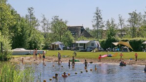 A lakeside scene with people swimming and playing near a campsite.