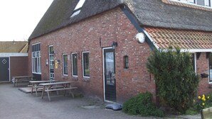 A brick building with a sloped roof, a door, and windows. There are picnic tables outside. - Farmhouse in Holwerd near the Sea (Holwerd)