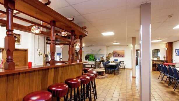 A restaurant with a bar area, high wooden ceiling, tiled floor, and a dining area with chairs and tables. - Farmhouse in Holwerd near the Sea (Holwerd)