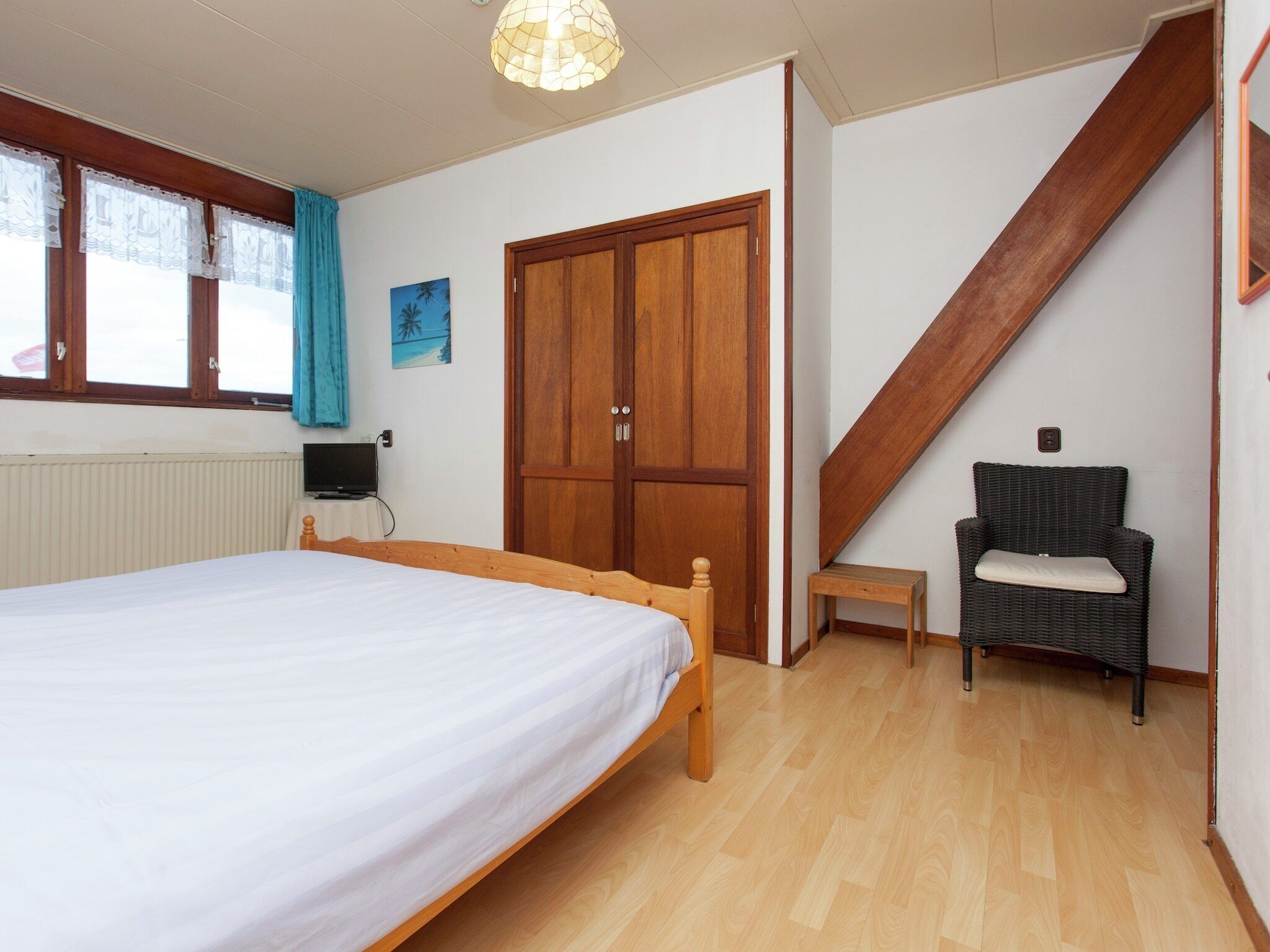 A bedroom with a bed, a wardrobe, a chair, a small table, and a staircase.