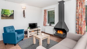 A living room with a sofa, a blue armchair, a coffee table, a fireplace, a television, and a painting on the wall. - Cozy House nr Drents-Friese (Hoogersmilde)