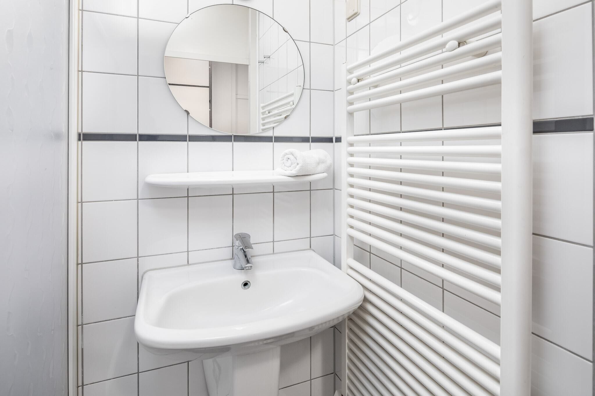 Un baño moderno con un lavamanos blanco, un espejo y un perchero para toallas.