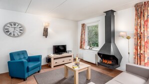 Una sala de estar con un sofá azul, un sofá color beige, una mesa de centro de madera, un televisor de pantalla plana, una chimenea y un reloj de pared.