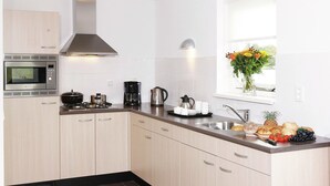 Una cucina moderna con forno a microonde integrato, piano cottura, macchina del caffè e un'ampia finestra con un vaso di fiori.