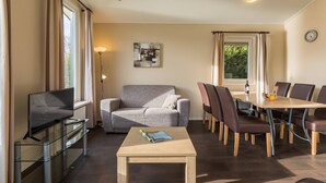 A modern living room with a sofa, a coffee table, a TV, and a dining area with chairs and a table.
