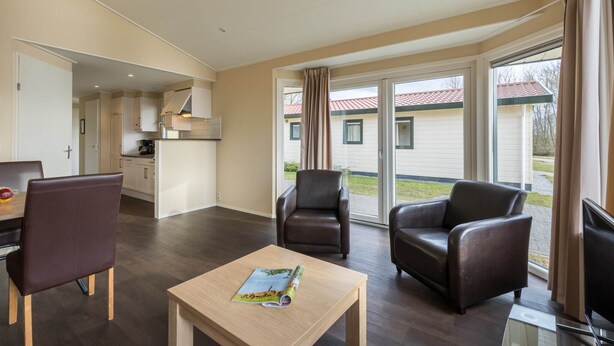 A modern living room with a dining area, a kitchen, and large sliding glass doors leading to a balcony.