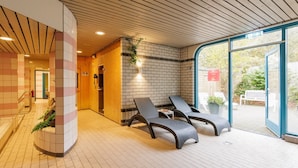 Et moderne opholdsområde indendørs med lounge-stole, en murstensvæg og en glasdør, der fører udendørs.