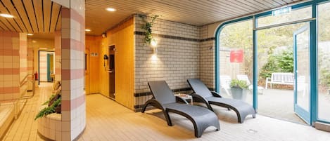 A modern indoor relaxation area with lounge chairs, a brick wall, and a glass door leading outside.