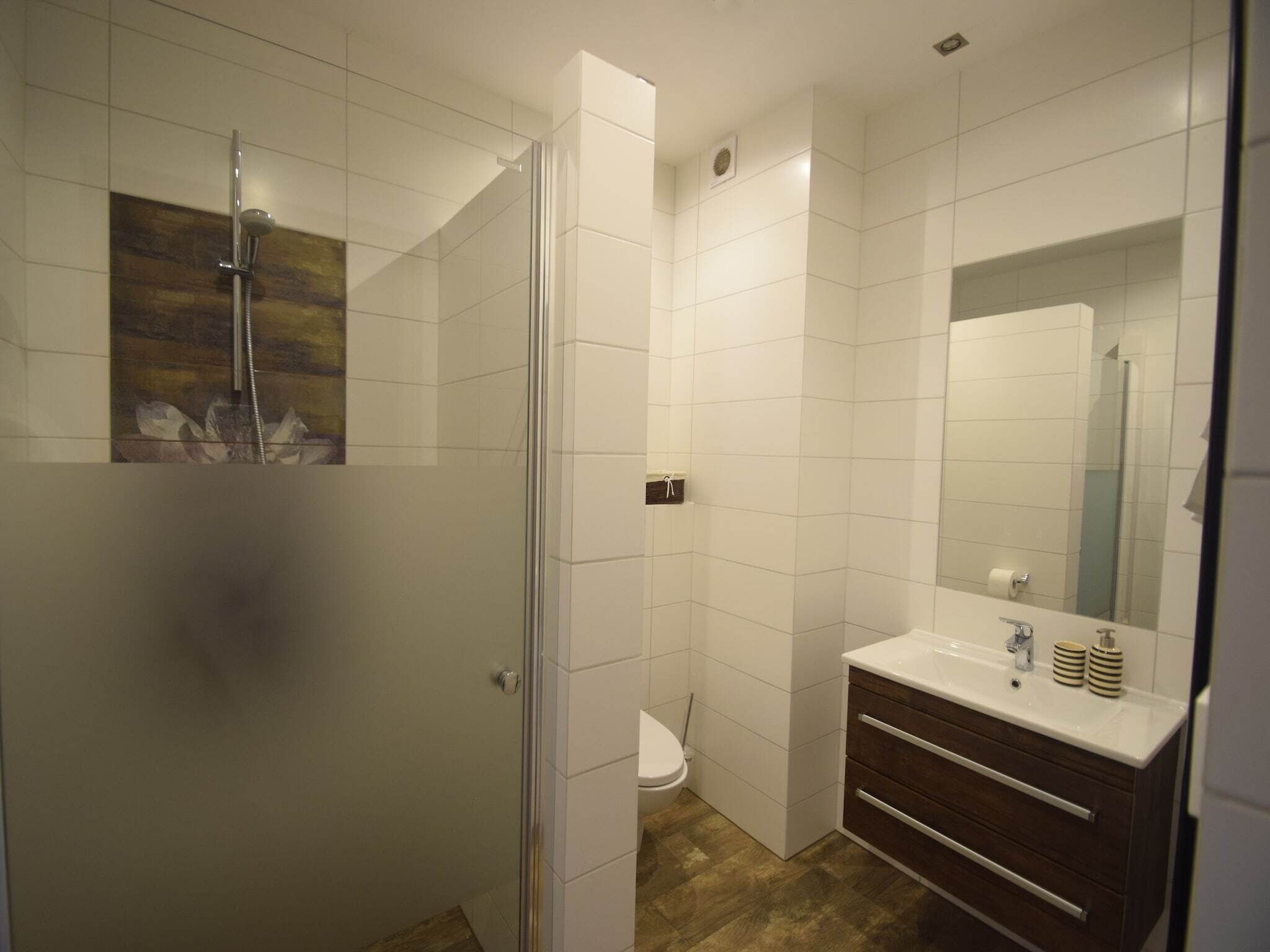 A modern bathroom with a glass shower enclosure, a toilet, and a vanity with a mirror.