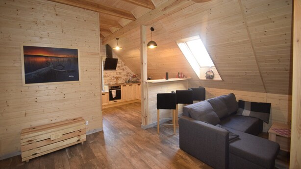 Un interno accogliente in legno con camera a soppalco, zona pranzo e soggiorno con divano e poltrone.