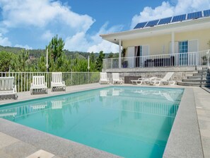 Ein Swimmingpool mit weißen Liegestühlen, einem weißen Zaun und einem Gebäude mit Solaranlagen.