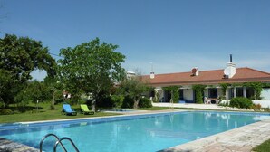 Une piscine dotée d’une plage en pierre, entourée d’une pelouse bien entretenue et d’une maison avec un toit en tuiles.