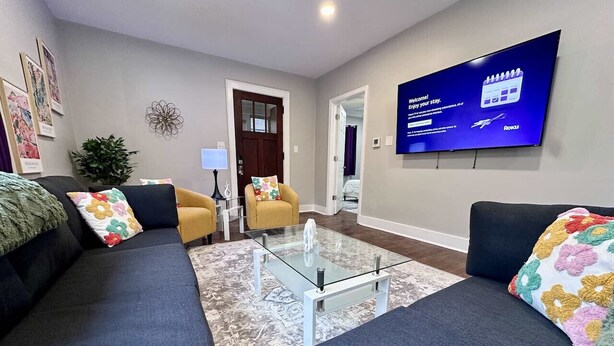 A modern living room with a glass coffee table, two sofas, a yellow armchair, and a flat-screen TV mounted on the wall. - Peaceful Giant House close to city (Carnegie)