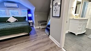 A bedroom with a bed, a desk, a chair, a dresser, and a bathroom with a sink and mirror. - Peaceful Giant House close to city (Carnegie)