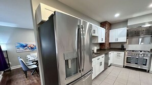 A modern kitchen with stainless steel appliances, white cabinets, and a dining area with a table and chairs. - Peaceful Giant House close to city (Carnegie)