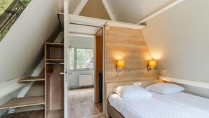 A bedroom with a bed, two wall-mounted lights, a wooden headboard, and a staircase leading to an outdoor area. - Bungalow in Bospark 't Wolfsven near Nature (Mierlo)