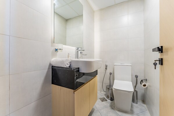 A modern bathroom with a black countertop sink, a mirror, a toilet, and a shower area.