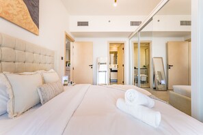 A hotel room with a large bed, a mirror, and a view of the bathroom and kitchen through an open door. - Community View 1BR with Balcony Near Downtown Dubai, Binghatti Avenue, Al Jaddaf (Dubai)