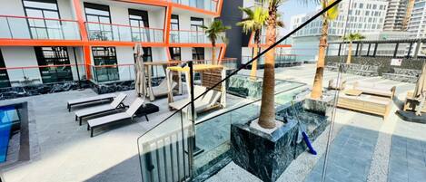 A modern outdoor pool area with lounge chairs, palm trees, and a glass railing.