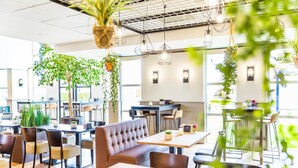 Un caffè moderno con diverse zone di seduta, tra cui una panca al centro e diversi tavoli con sedie.