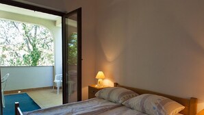 A bedroom with a bed, a nightstand, a lamp, and a view of the outside.
